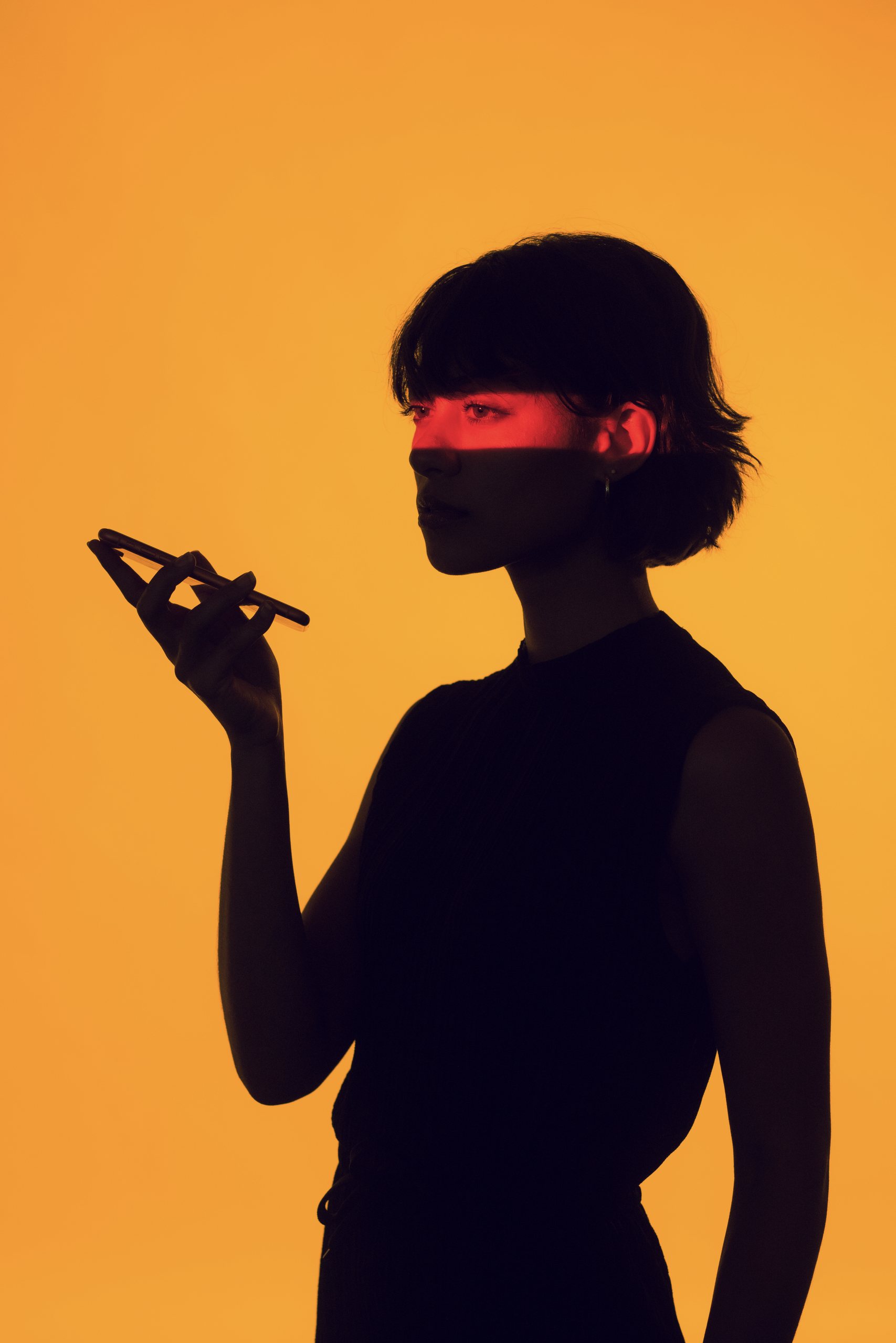 Woman in red light holding a phone against an orange backdrop