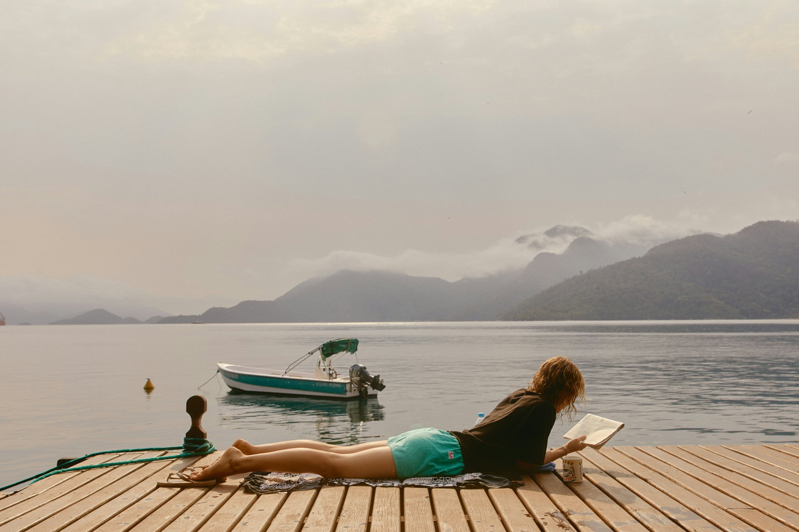 Woman reading on a dock beside a lake and mountains