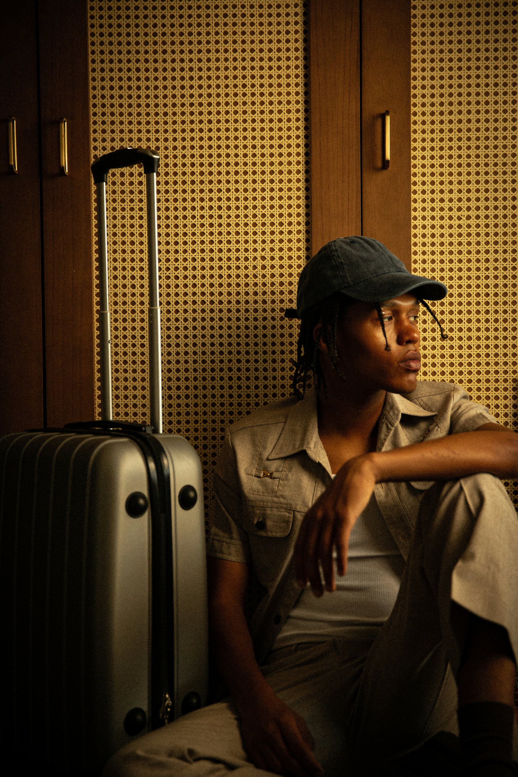 Traveller resting beside a suitcase against a cane wall